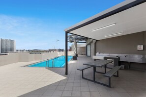 Un área de piscina en la azotea con piscina, bancos y vistas de la ciudad.