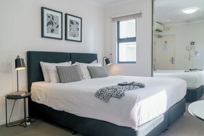 A hotel room with a large bed, bedside lamps, a round table, and two framed artworks on the wall. - Gabba Central Apartments (Woolloongabba)