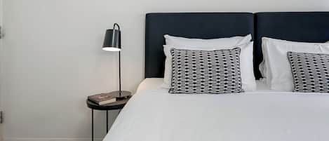 Una habitación de hotel con una cama, dos almohadas, una mesita de noche con lámpara y una obra de arte abstracta enmarcada en la pared.