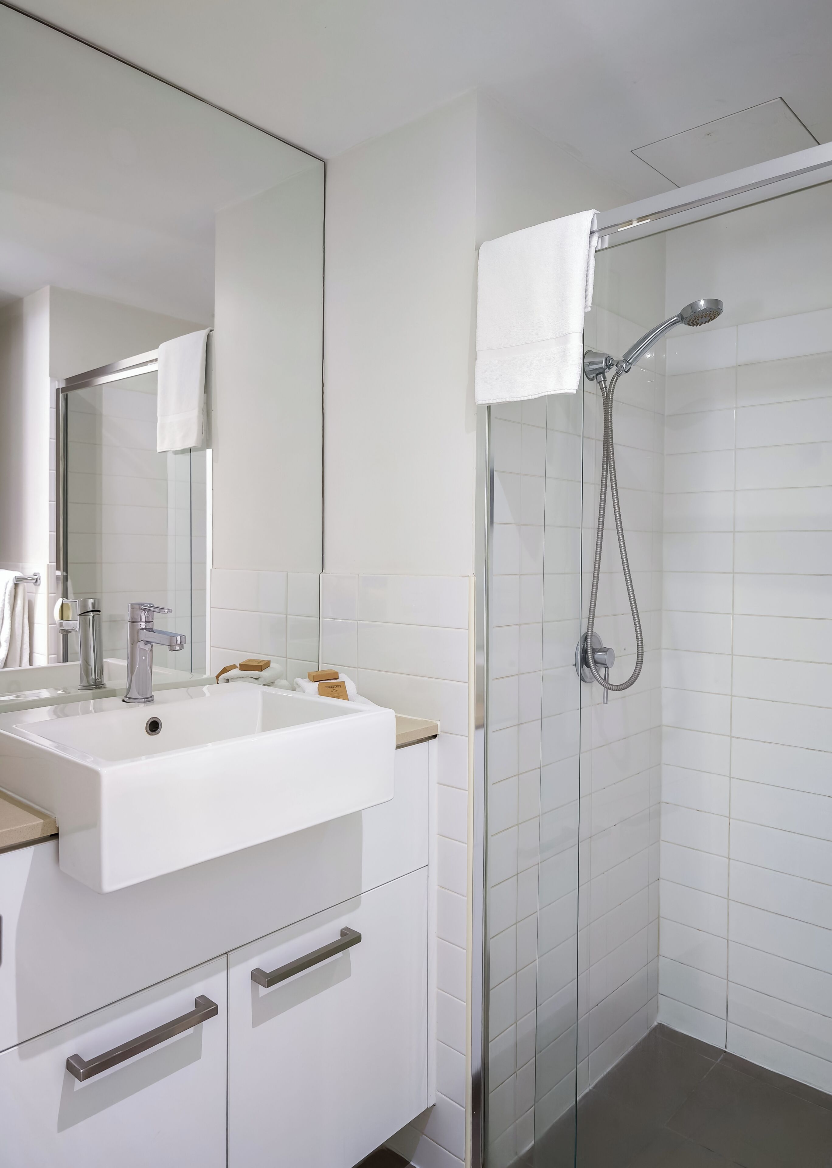 Un baño moderno con lavamanos, espejo y ducha blancos.