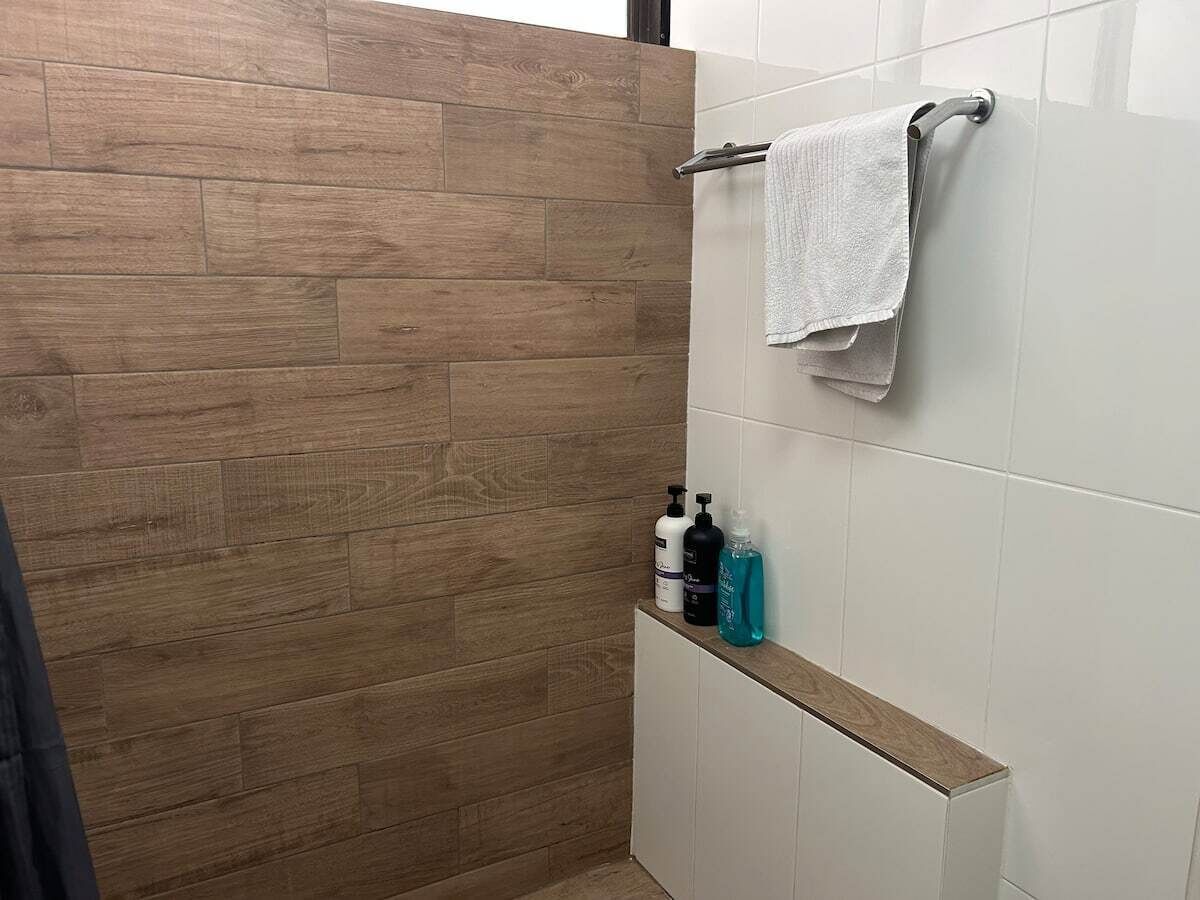 A bathroom with wooden wall tiles, a white tiled wall, a towel rack with a white towel, and a shelf with toiletries.