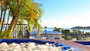 A pool area with a view of the sea, palm trees, and a building with a blue roof. - Whitsunday Terraces Hotel Airlie Beach (Airlie Beach)