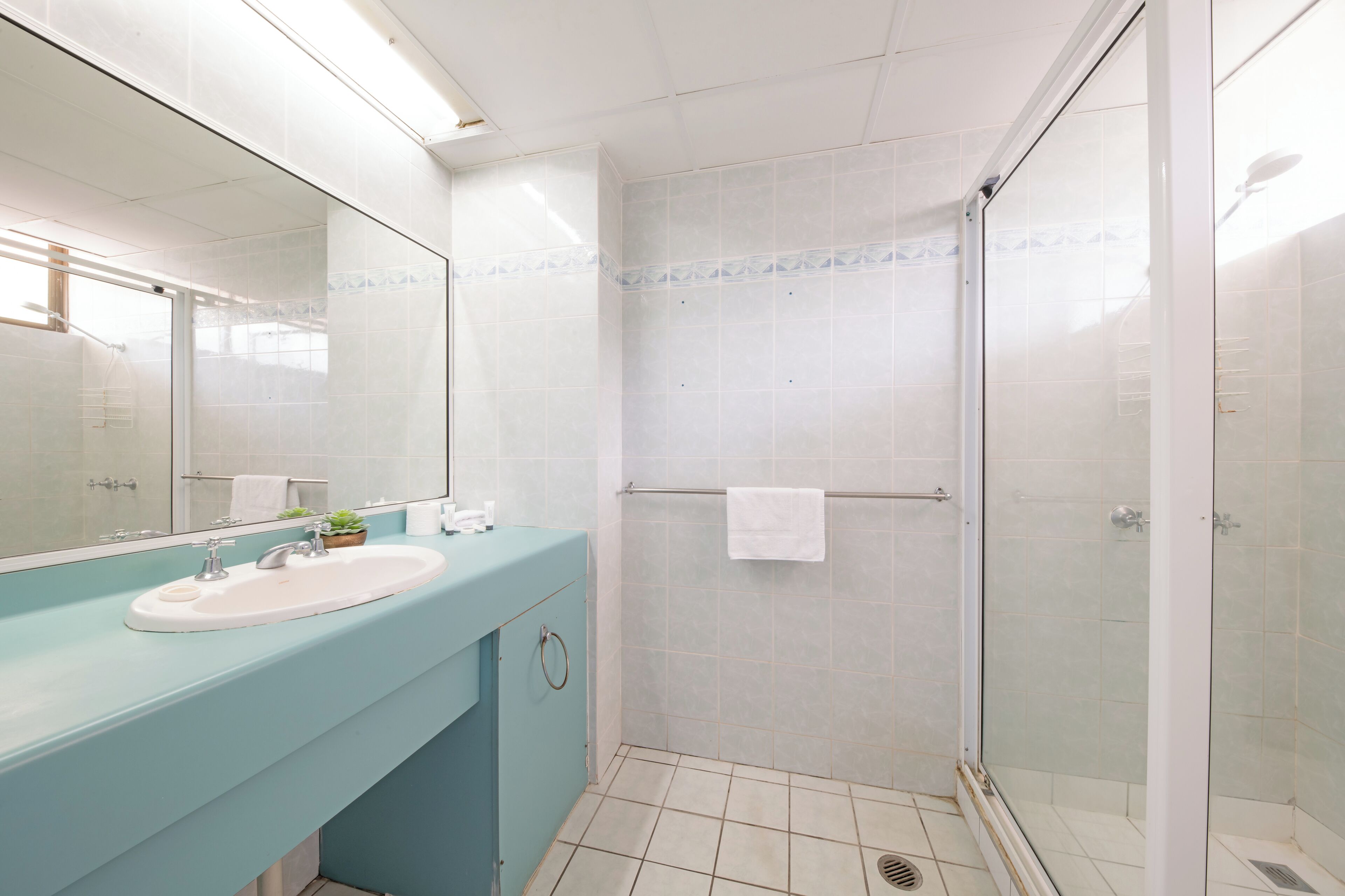 A bathroom with a blue countertop, a white sink, a glass-enclosed shower, and a tiled floor.