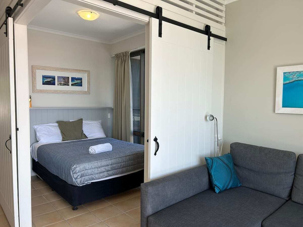 Un dormitorio con cama, sofá gris y puerta corredera.