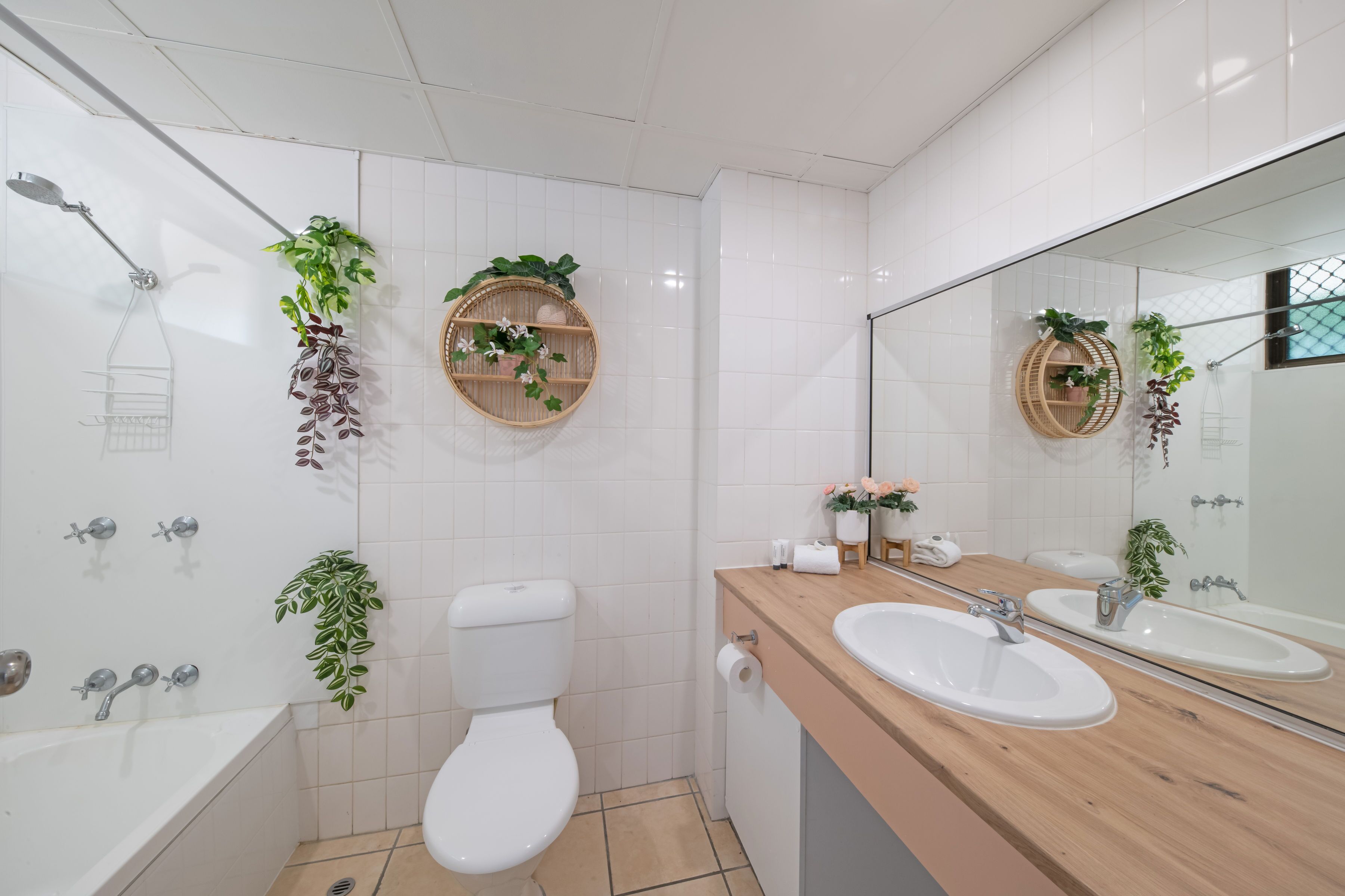 A modern bathroom with a bathtub, two sinks, a toilet, and decorative plants.