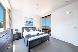 Un dormitorio moderno con una cama grande, una mesita de noche, un aparador y vistas al océano a través de un ventanal corredera.