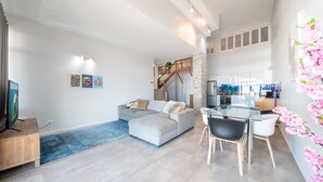A modern living room with a grey sofa, a glass dining table, and a staircase leading to an upper level. - Whitsunday Terraces Hotel Airlie Beach (Airlie Beach)
