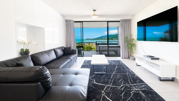 A modern living room with a black leather sofa, a white coffee table, and a large TV on the wall. - Whitsunday Terraces Hotel Airlie Beach (Airlie Beach)