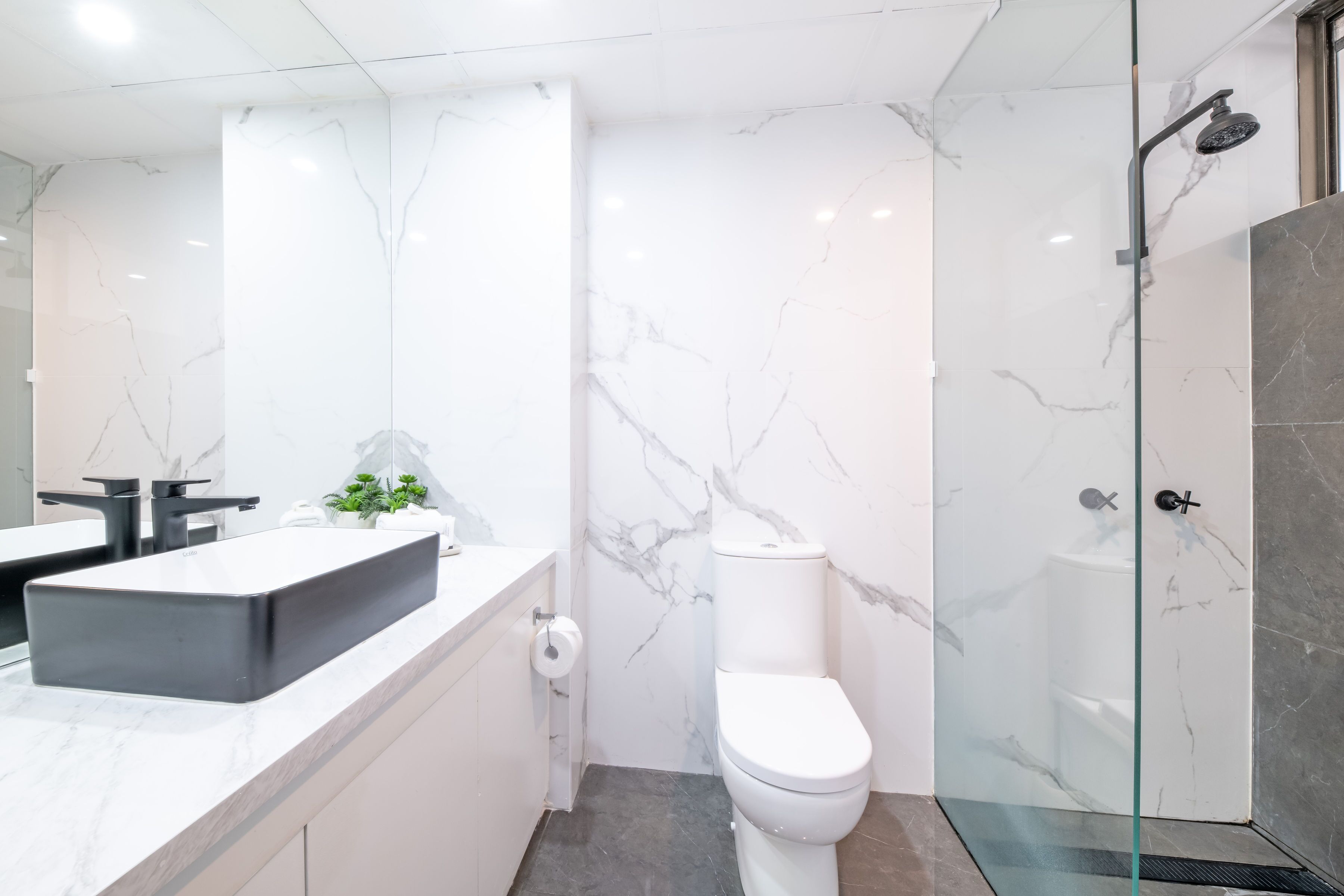 A modern bathroom with a large mirror, a rectangular sink, a toilet, and a glass-enclosed shower area.