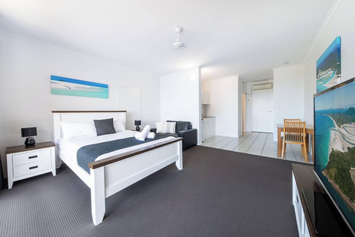 A modern hotel room with a large bed, a desk, a chair, and a television.