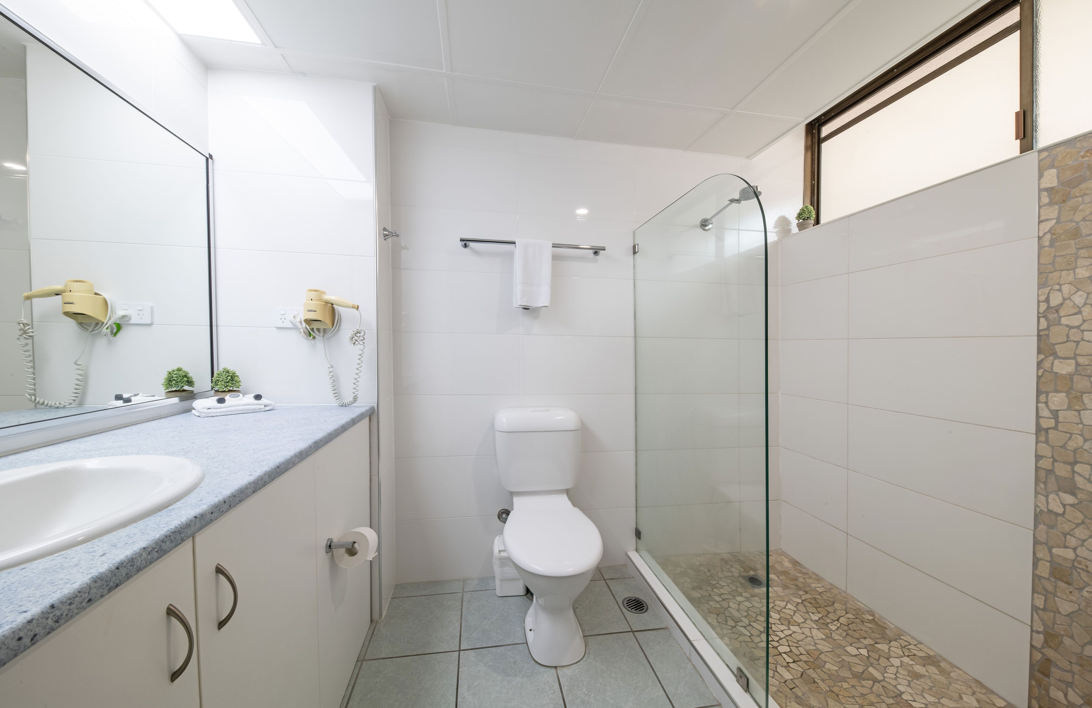 A modern bathroom with a glass shower enclosure, a white toilet, and a large sink with a mirror.