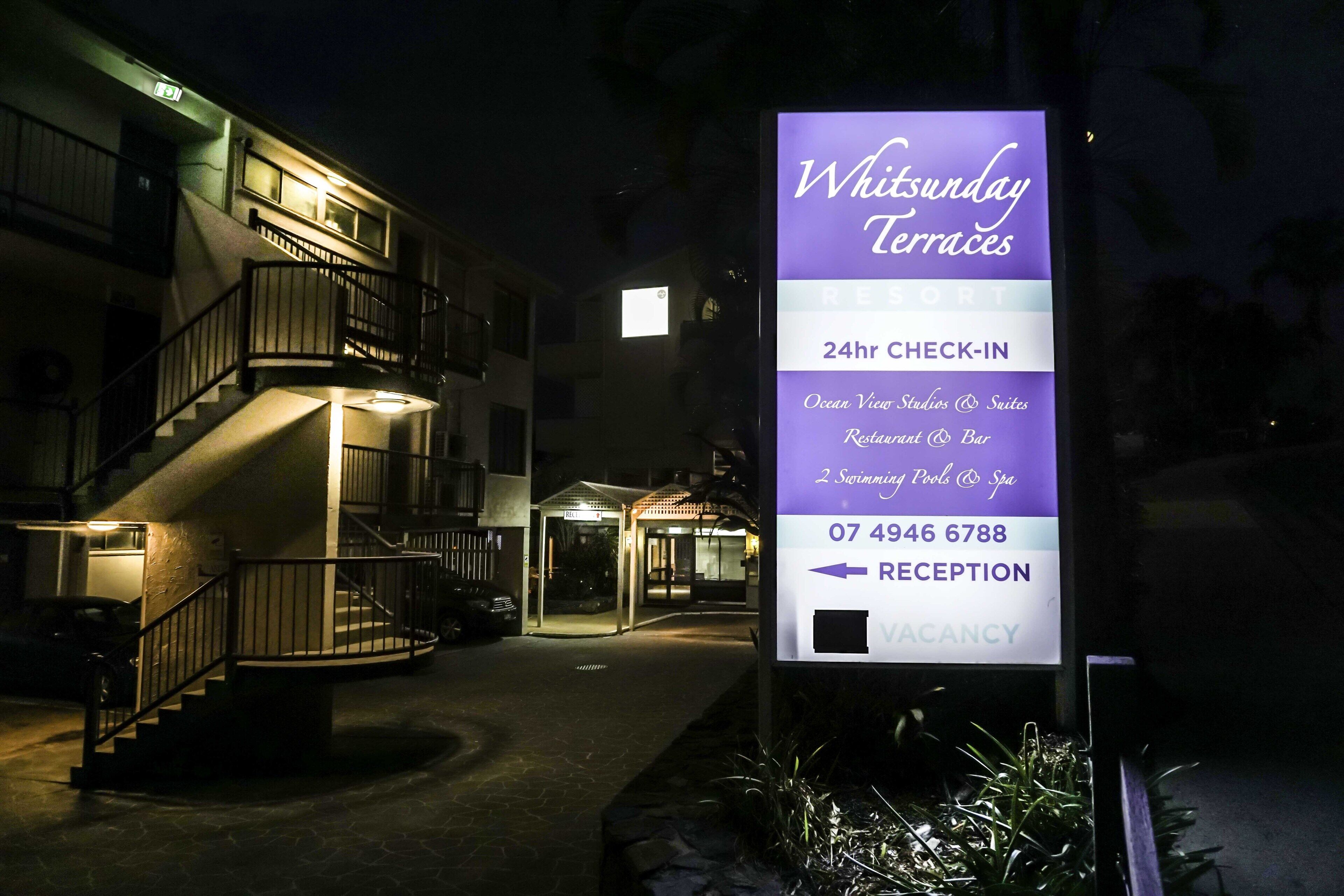 Une enseigne d’hôtel indiquant « Witsunday Terraces » et mentionnant les équipements suivants : « Studios et suites avec vue sur l’océan », « Restaurant et bar », « 2 piscines et spa », ainsi qu’un service d’enregistrement ouvert 24 heures sur 24.