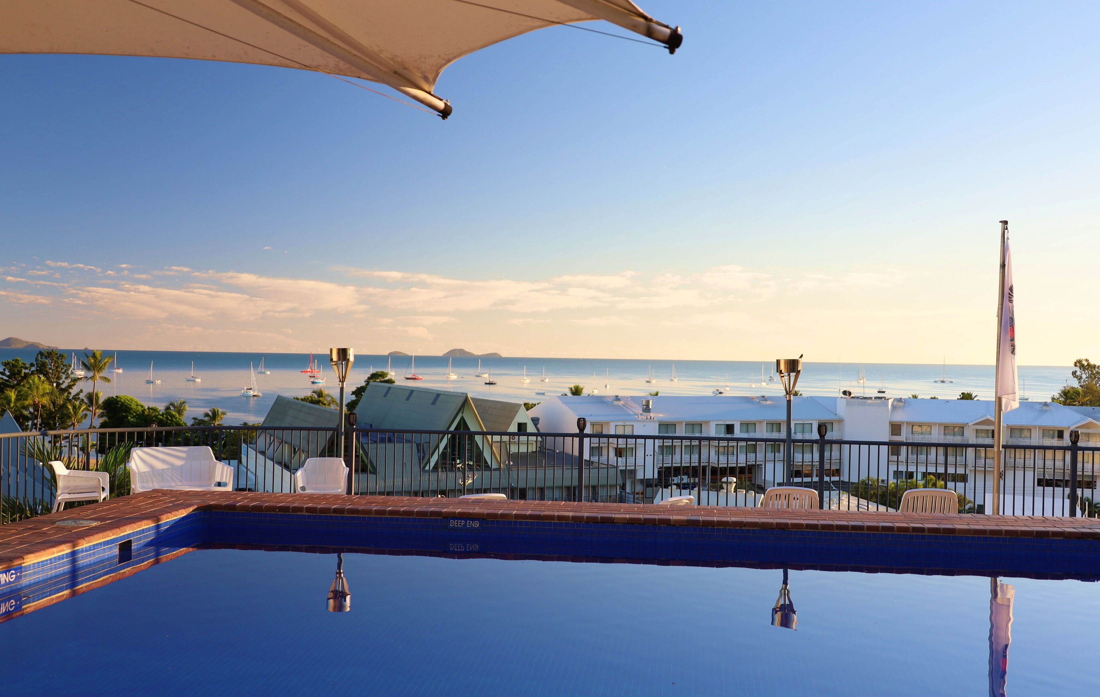 A poolside view with a clear view of the ocean and boats in the distance.