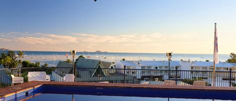 A poolside view with a clear view of the ocean and boats in the distance.