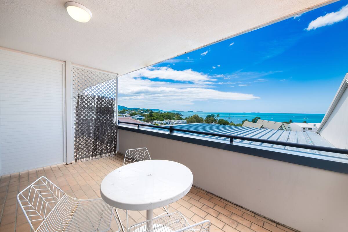 A balcony with a white table and chairs, a view of the sea, and a patterned fence.