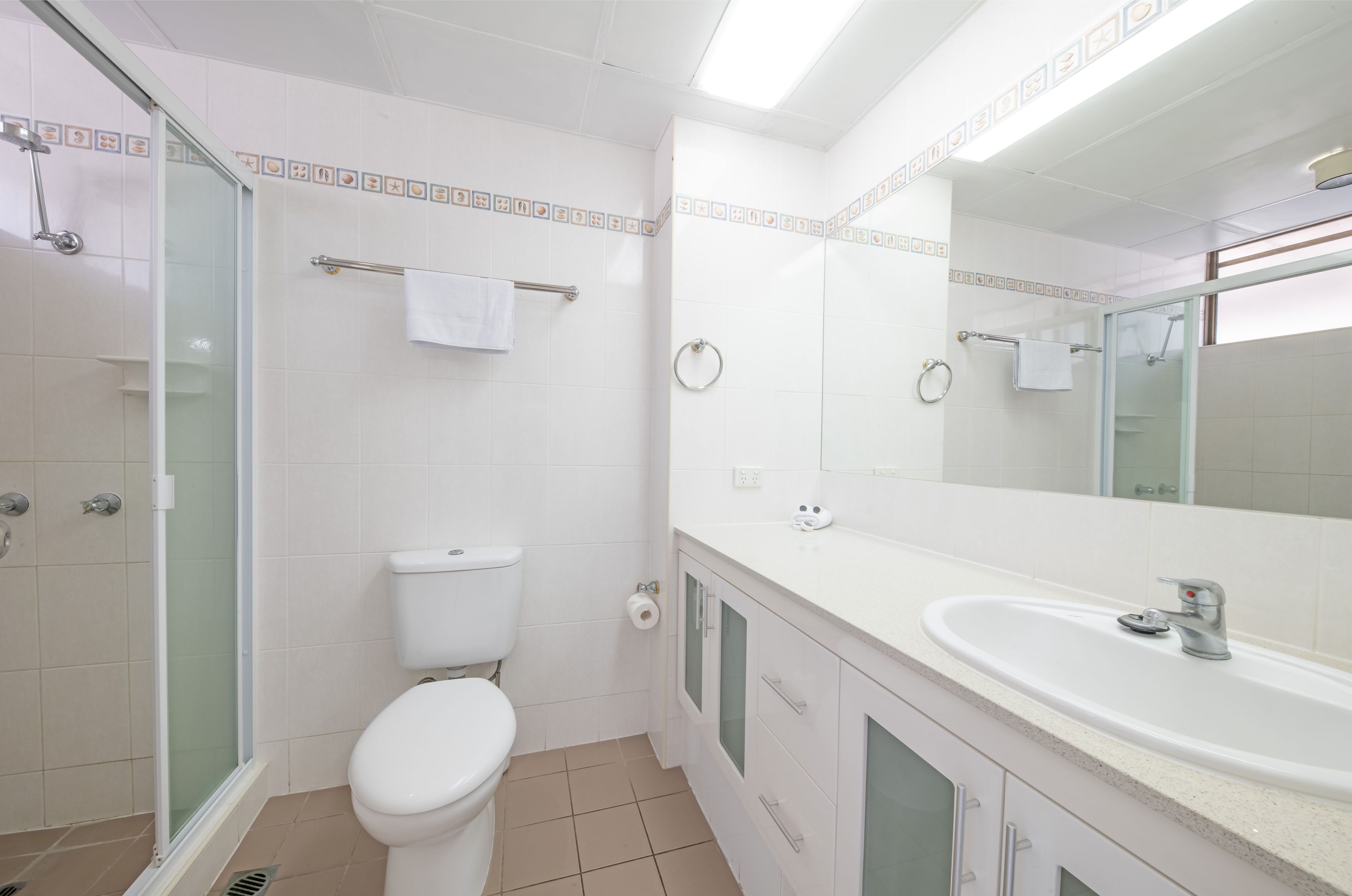 Un baño moderno con cabina de ducha de vidrio, un inodoro blanco, un lavamanos con espejo y un perchero para toallas.