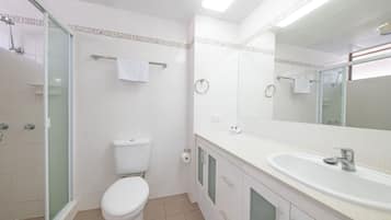 Un baño moderno con cabina de ducha de vidrio, un inodoro blanco, un lavamanos con espejo y un perchero para toallas.