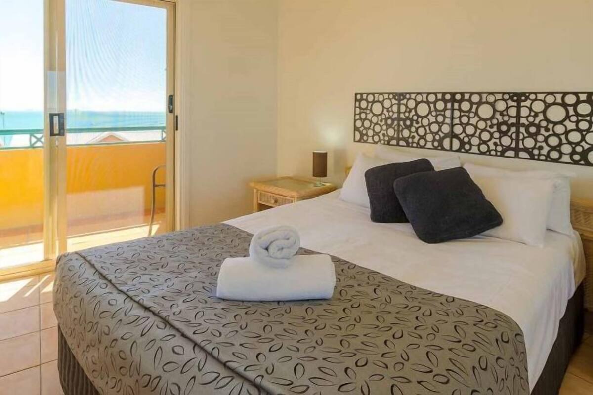 A hotel room with a bed, a nightstand, a chair, and a balcony with a view.