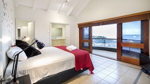 A bedroom with a bed, a desk, a chair, a TV, and a balcony with a view. - Toscana Village Resort (Airlie Beach)