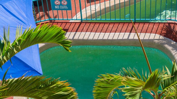A woman in a bikini standing in a clear pool surrounded by palm trees and a blue umbrella. - Toscana Village Resort (Airlie Beach)