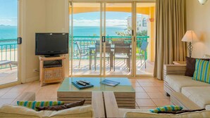 A hotel room with a balcony, a television, a sofa, a coffee table, and a view of the sea. - Toscana Village Resort (Airlie Beach)