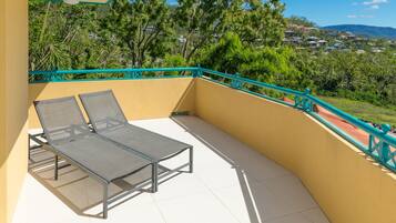 A balcony with two metal-framed chairs and a small table, overlooking a residential area with trees and houses.