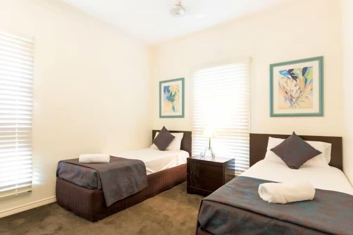 A hotel room with two beds, a nightstand, and artwork on the walls.