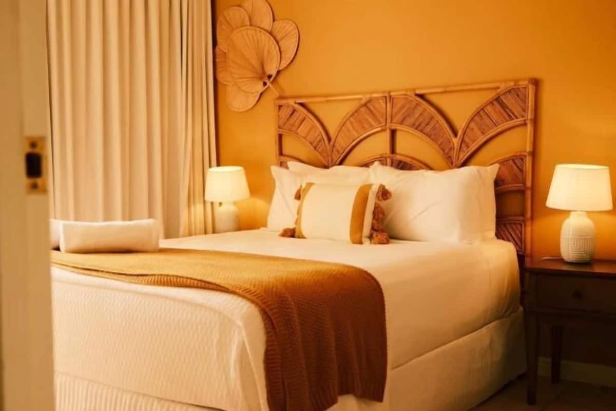 A hotel room with a large bed, two bedside tables with lamps, a decorative wall headboard, and a large window with curtains.