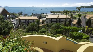 A coastal hotel with multiple buildings, a view of the sea with boats, and lush greenery. - Toscana Village Resort (Airlie Beach)