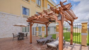 A covered outdoor seating area with a pergola, a table with chairs, and a lawn chair. - Sleep Inn And Suites Pearland - Houston South (Pearland)