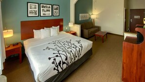 A hotel room with a large bed, a sofa, a desk, and a mirror. - Sleep Inn And Suites Pearland - Houston South (Pearland)