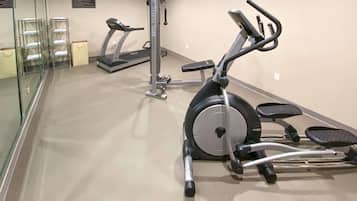 Gimnasio de hotel con máquinas de cardio, equipo de pesas y una pared de vidrio.