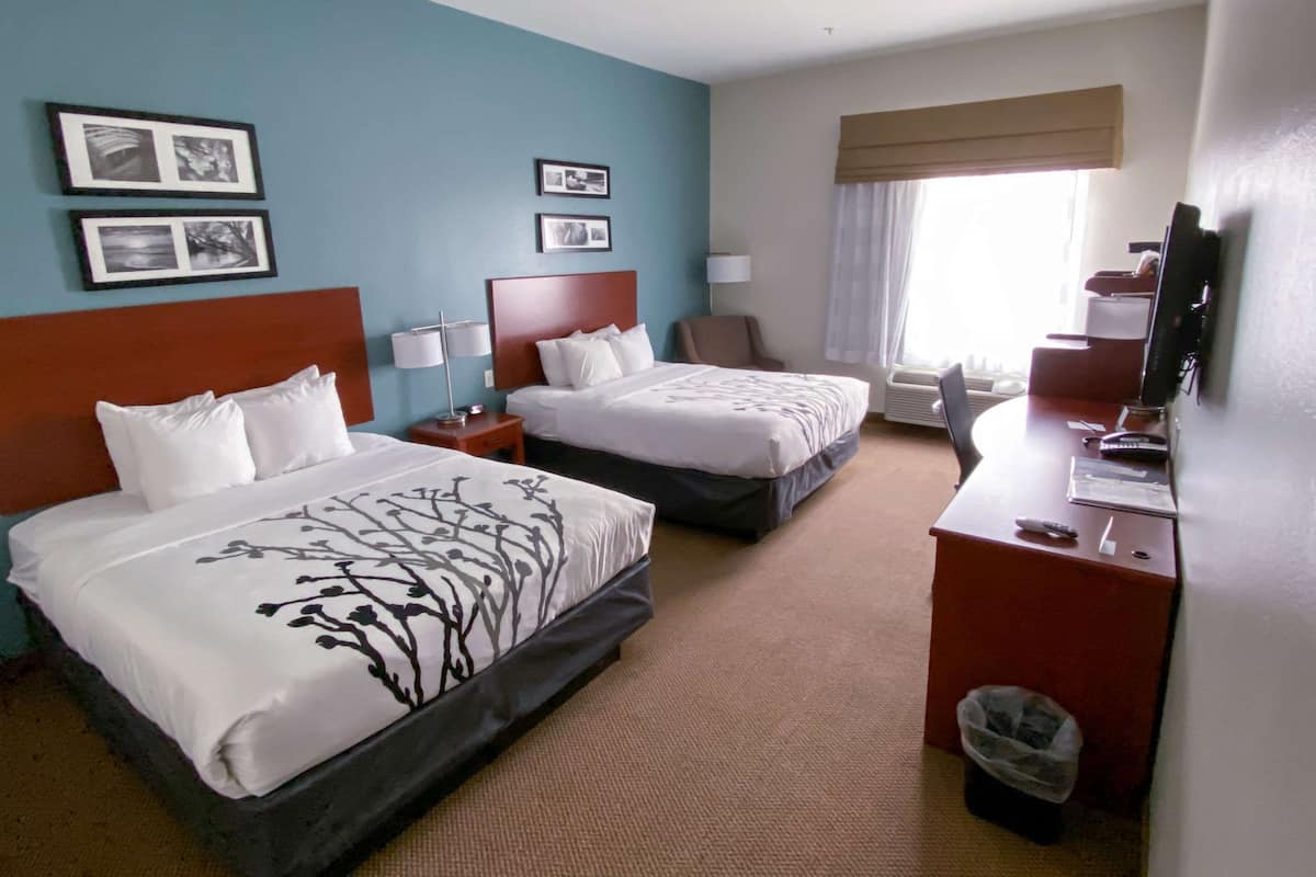 A hotel room with two beds, a desk, a chair, a TV, and framed pictures on the wall.