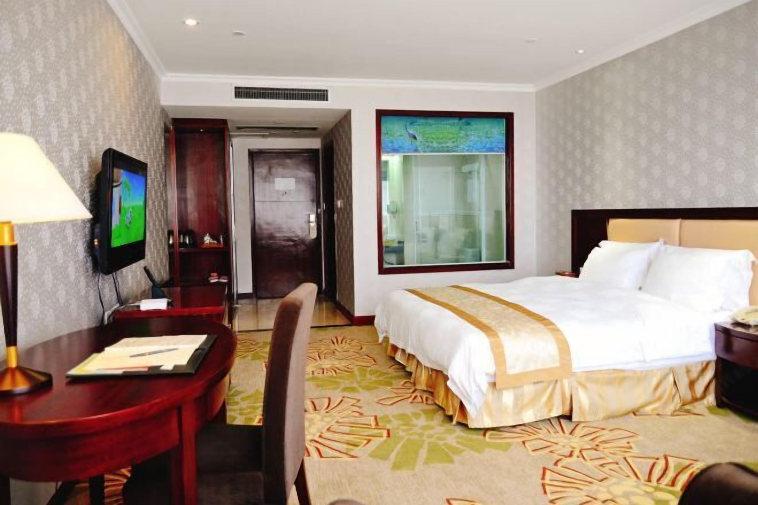 A hotel room with a bed, desk, chair, TV, and a window with a view.