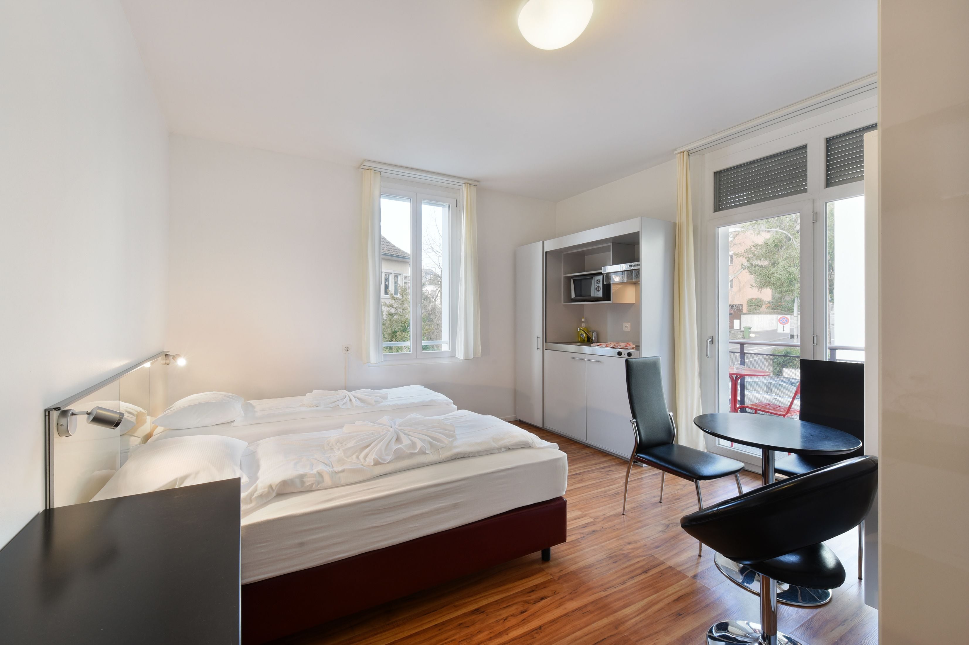 Una habitación de hotel moderna con cama, escritorio, silla, una mesita y un kitchenette.
