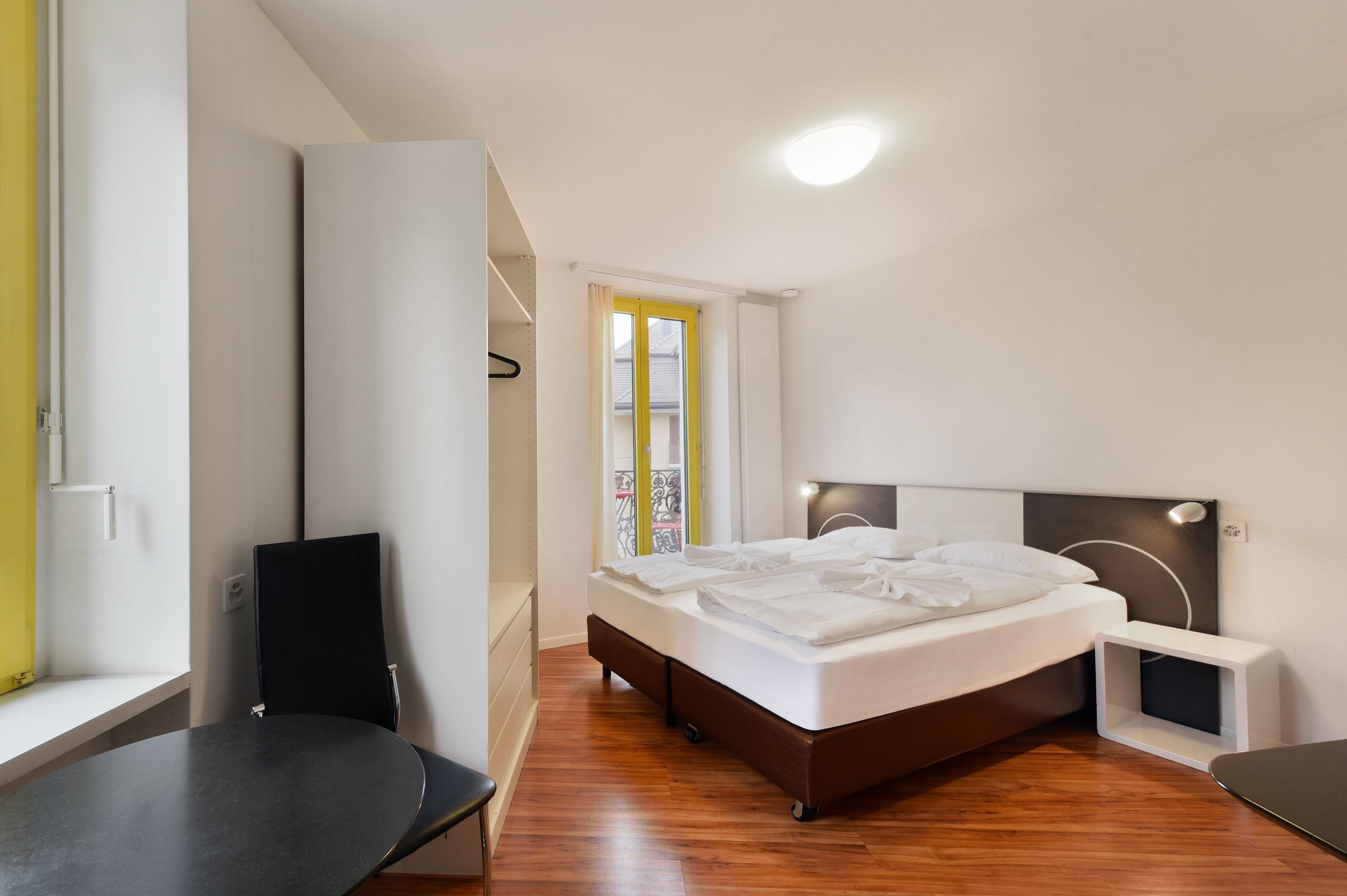 A modern bedroom with a bed, a chair, a desk, and a window with curtains.