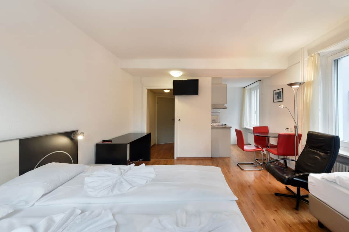 A hotel room with a bed, a desk, a chair, and a small kitchenette.