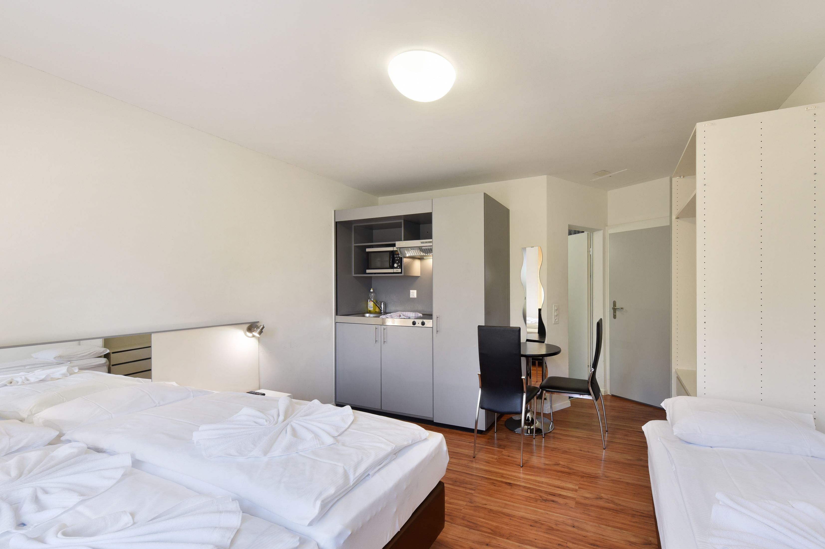 Hotellihuone, jossa on kaksi sänkyä, pieni keittiö, ruokailutila ja kylpyhuone.