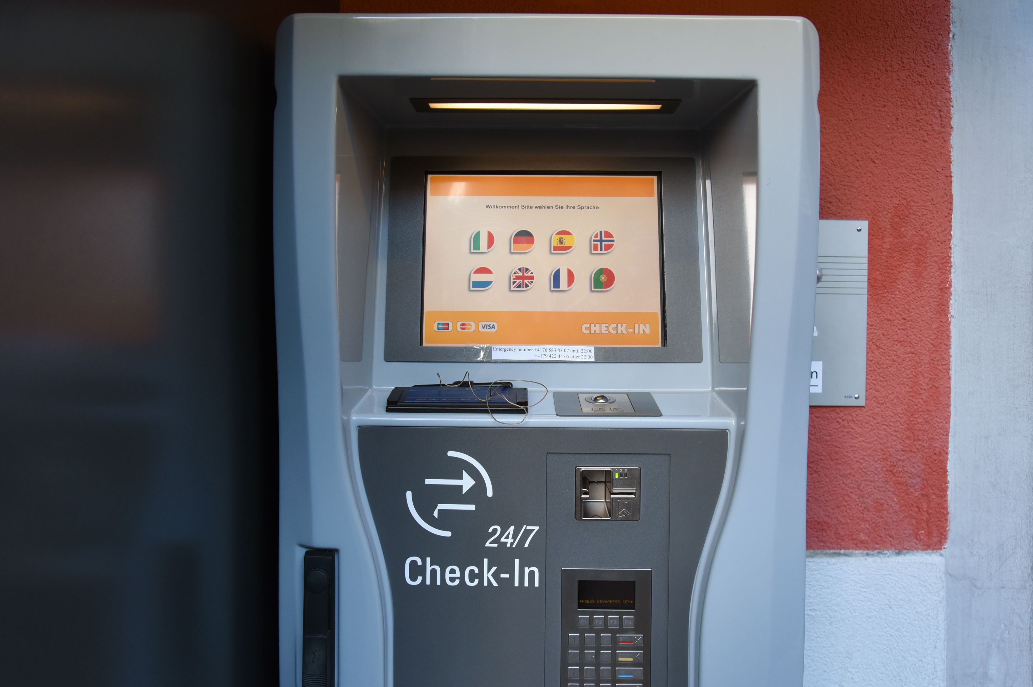 A 24/7 check-in self-service kiosk with a screen displaying language options and a keypad below.