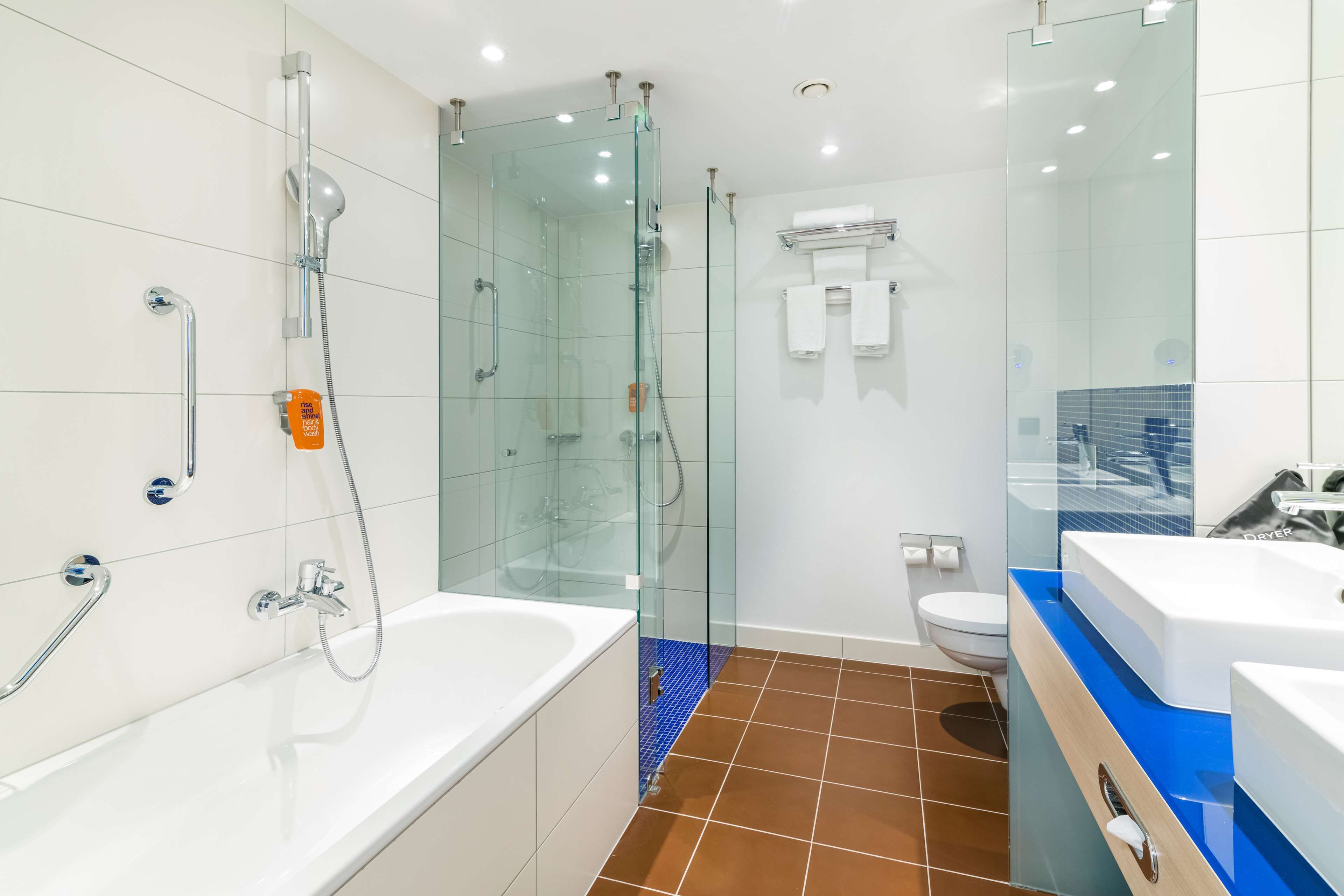 A modern bathroom with a glass-enclosed shower, a white bathtub, and a blue-tiled floor.