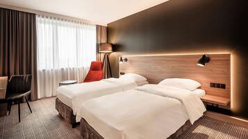A hotel room with two beds, a desk, a chair, and a lamp.