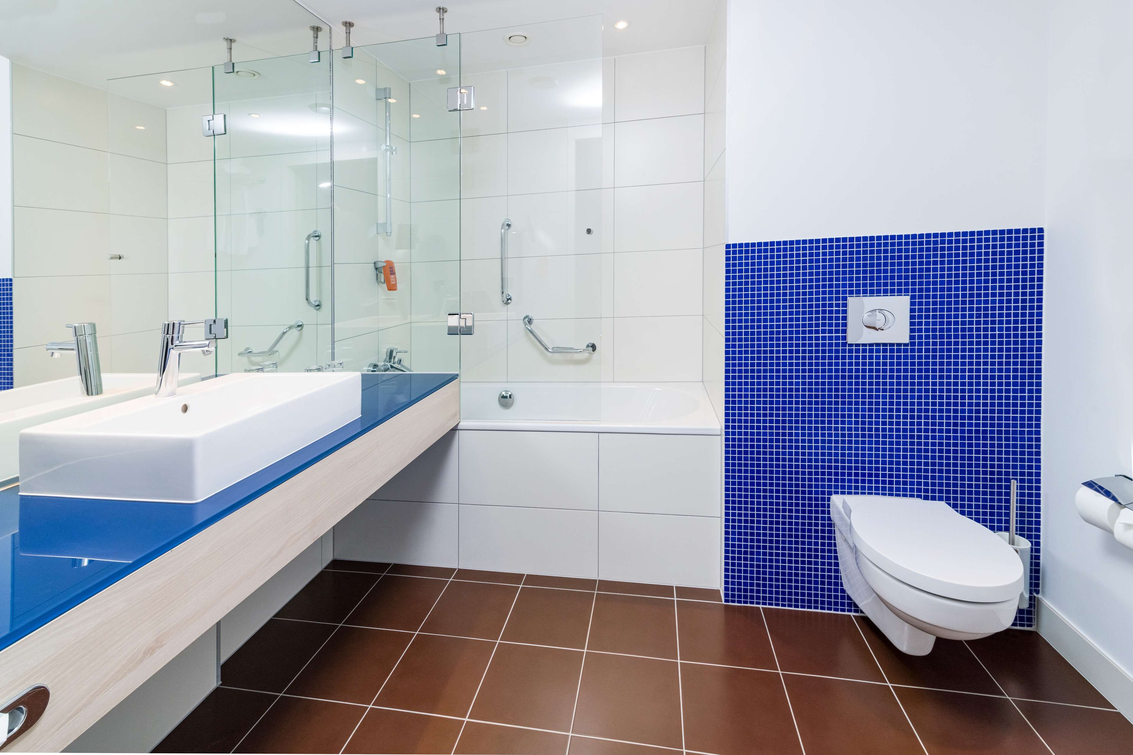 A modern bathroom with a glass-enclosed shower, a white bathtub, and a toilet.