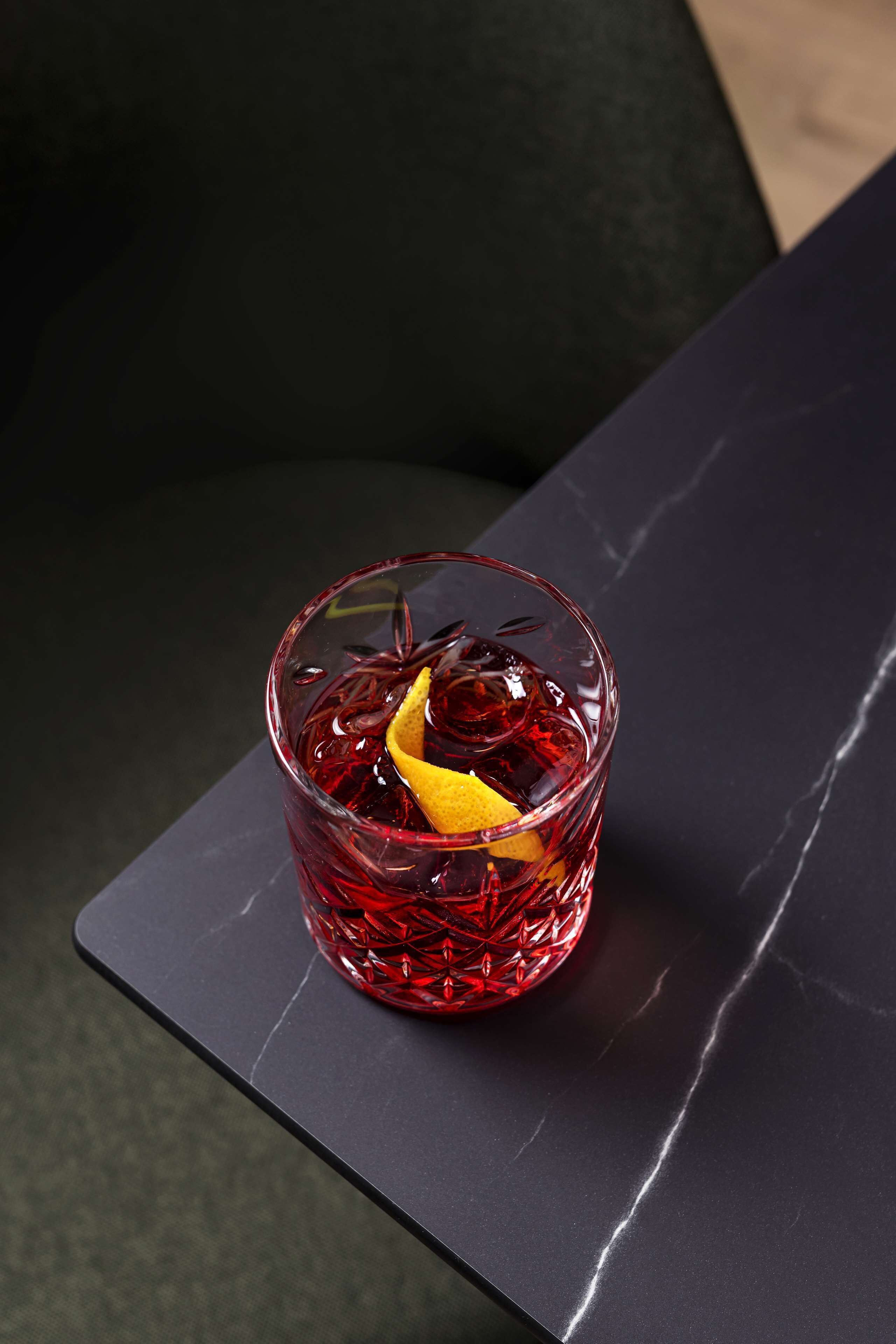 Ein Glas rotes Getränk mit einer Zitronenscheibe auf dunklem Untergrund.