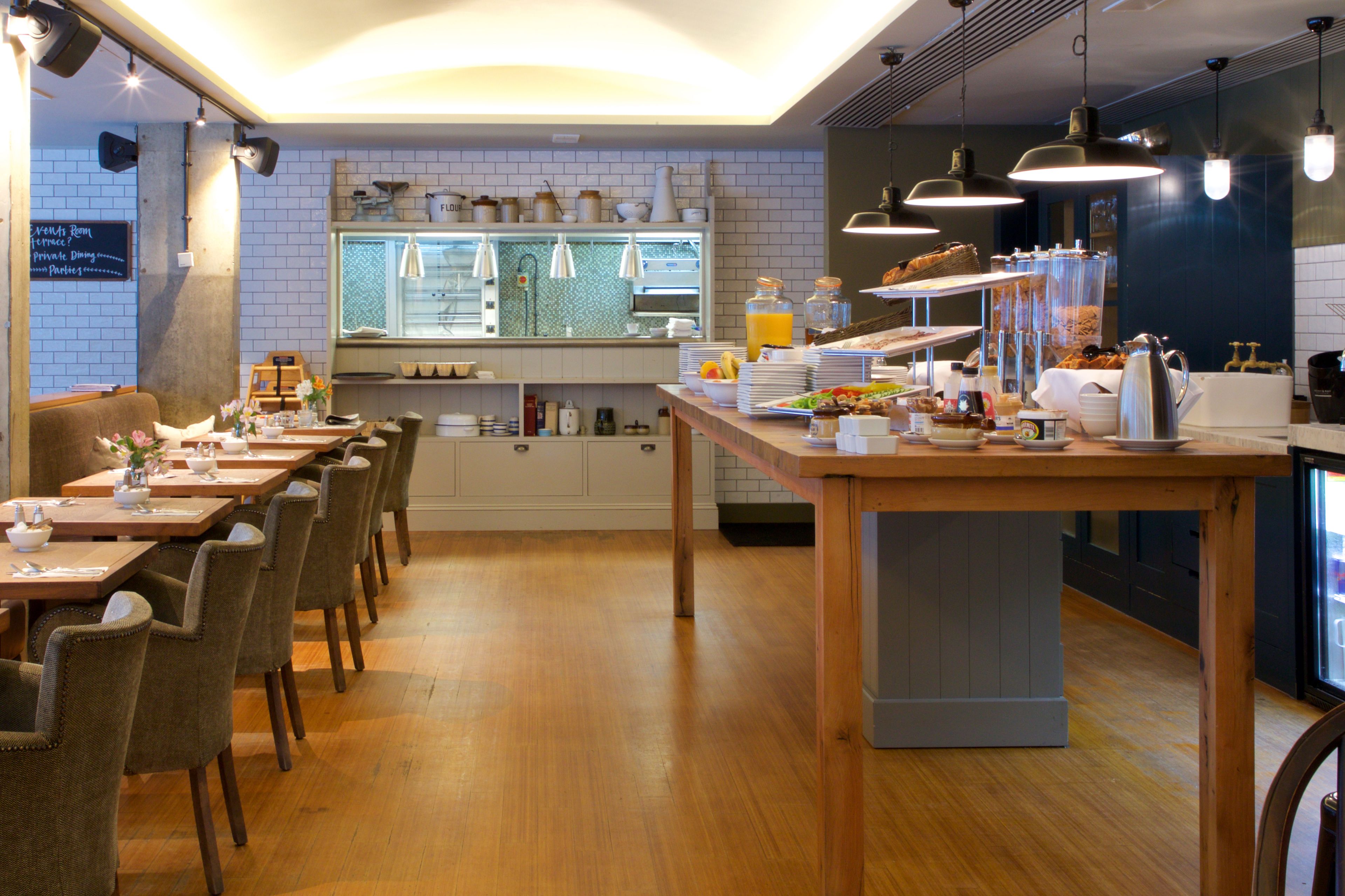 A restaurant with wooden tables and chairs, a kitchen area, and a counter with food and drinks.