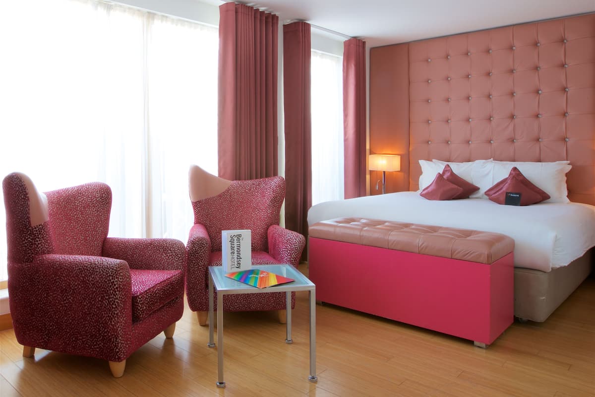Une chambre d’hôtel avec un lit, deux chaises, une petite table et une fenêtre avec des rideaux.