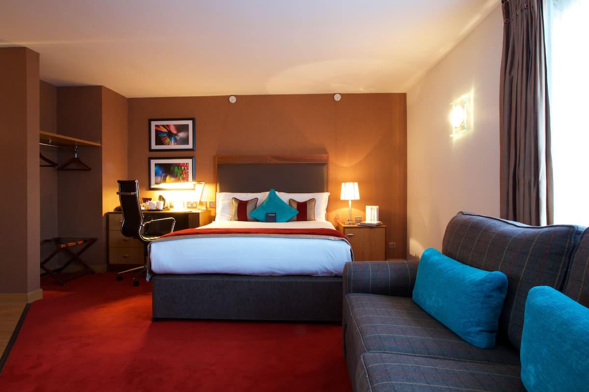 Une chambre d’hôtel avec un grand lit, un canapé, un bureau avec une chaise et une armoire.