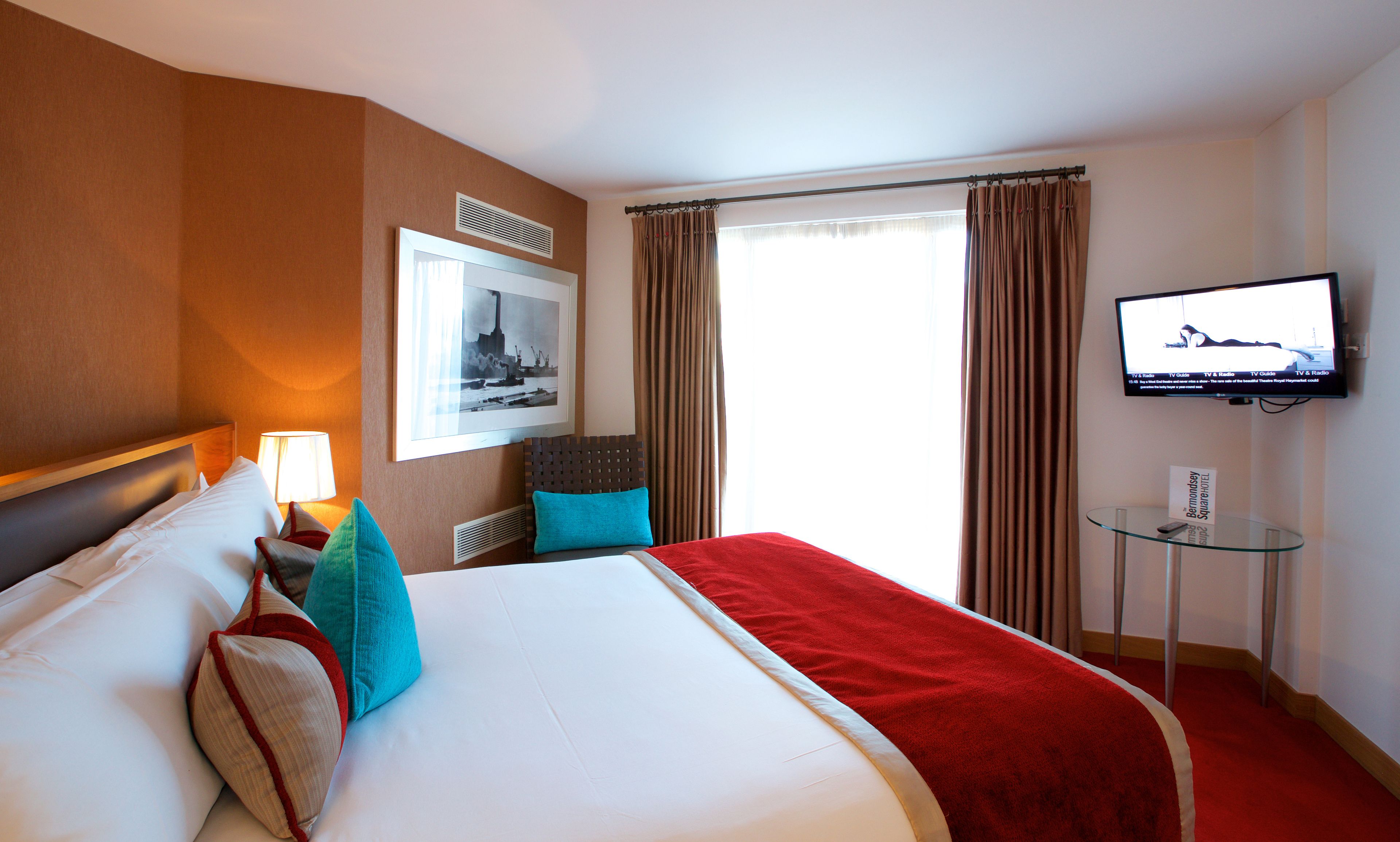 Habitación de hotel con una cama grande, televisión, un cuadro en la pared y una ventana con cortinas.