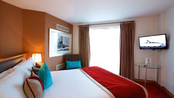 Habitación de hotel con una cama grande, televisión, un cuadro en la pared y una ventana con cortinas.