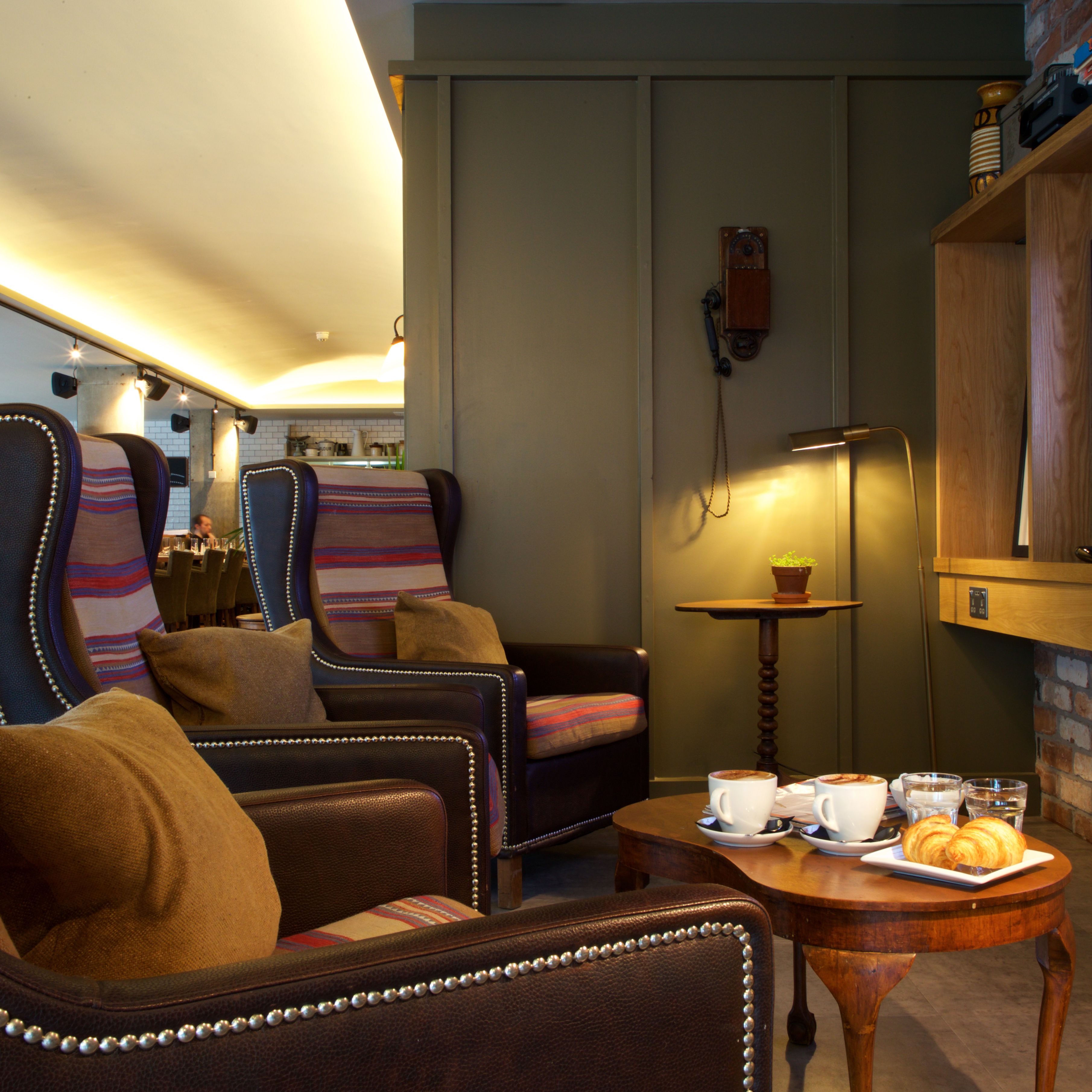 A cozy seating area with leather armchairs and a wooden coffee table, featuring a plate of croissants and cups.