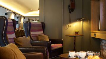 A cozy seating area with leather armchairs and a wooden coffee table, featuring a plate of croissants and cups.